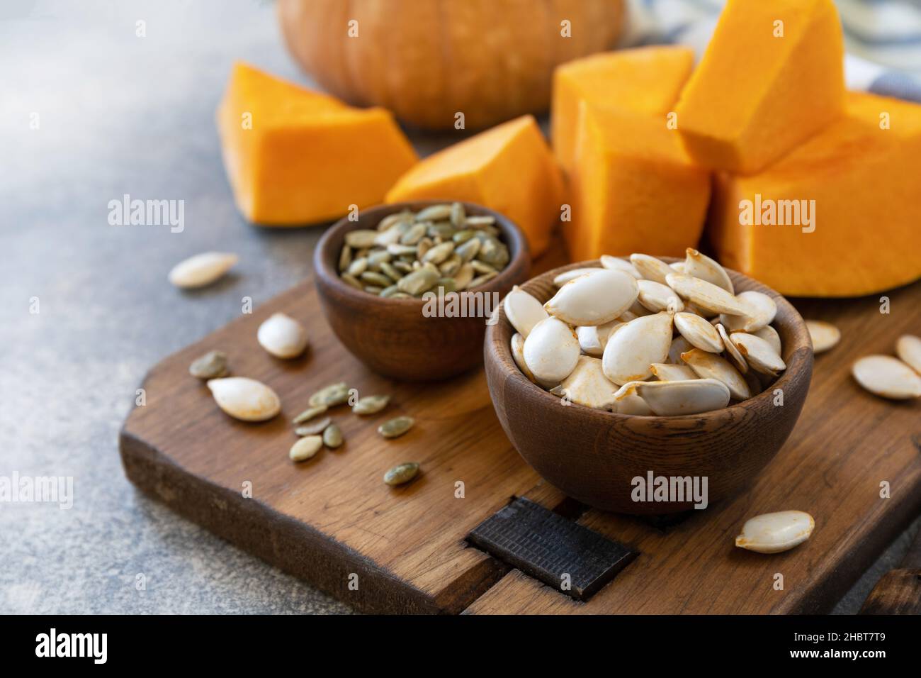 Semi di zucca grezzi supercrudi dopo il raccolto. Semi di zucca in ciotola di legno su sfondo di pietra grigia. Spazio di copia. Foto Stock