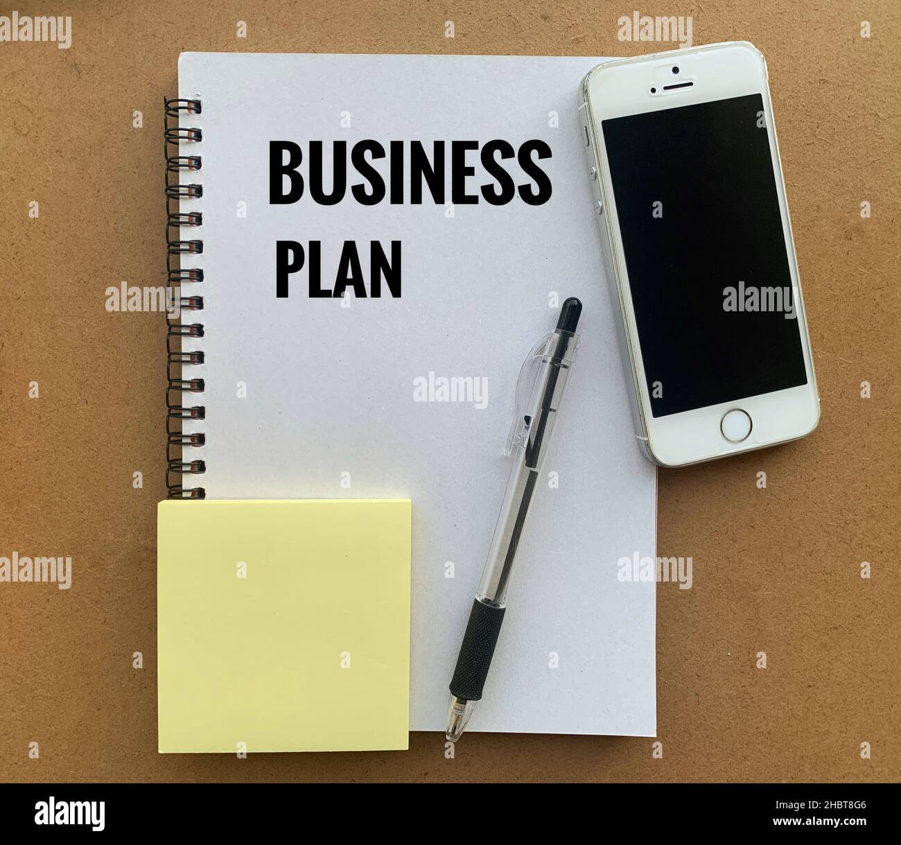 Testo del piano aziendale su appunti con smartphone, penna, tavolo marrone e sfondo adesivo. Concetto aziendale Foto Stock