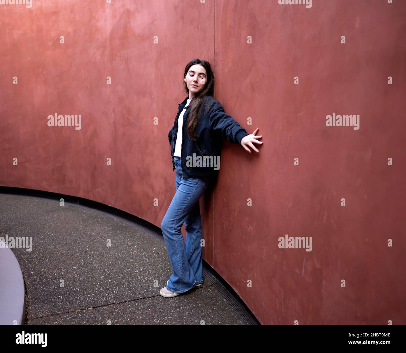 Adolescente donna appoggiata contro un muro colorato Rust Foto Stock