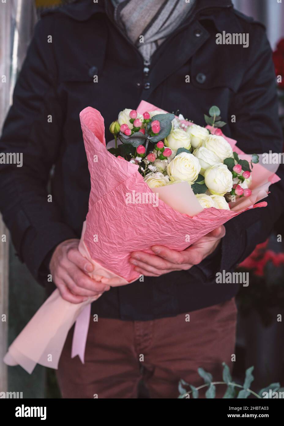 Giovane uomo che tiene bel bouquet di fiori primo piano. Uomo che indossa giacca calda e sciarpa. Persone irriconoscibili. Foto ritagliata in verticale, Foto Stock