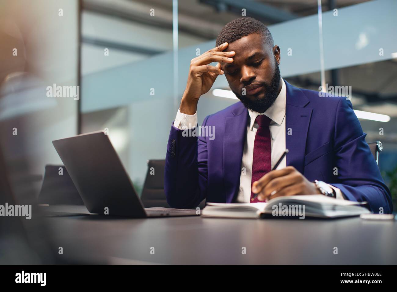 Pensivo uomo nero CEO che lavora in ufficio, prendendo appunti Foto Stock
