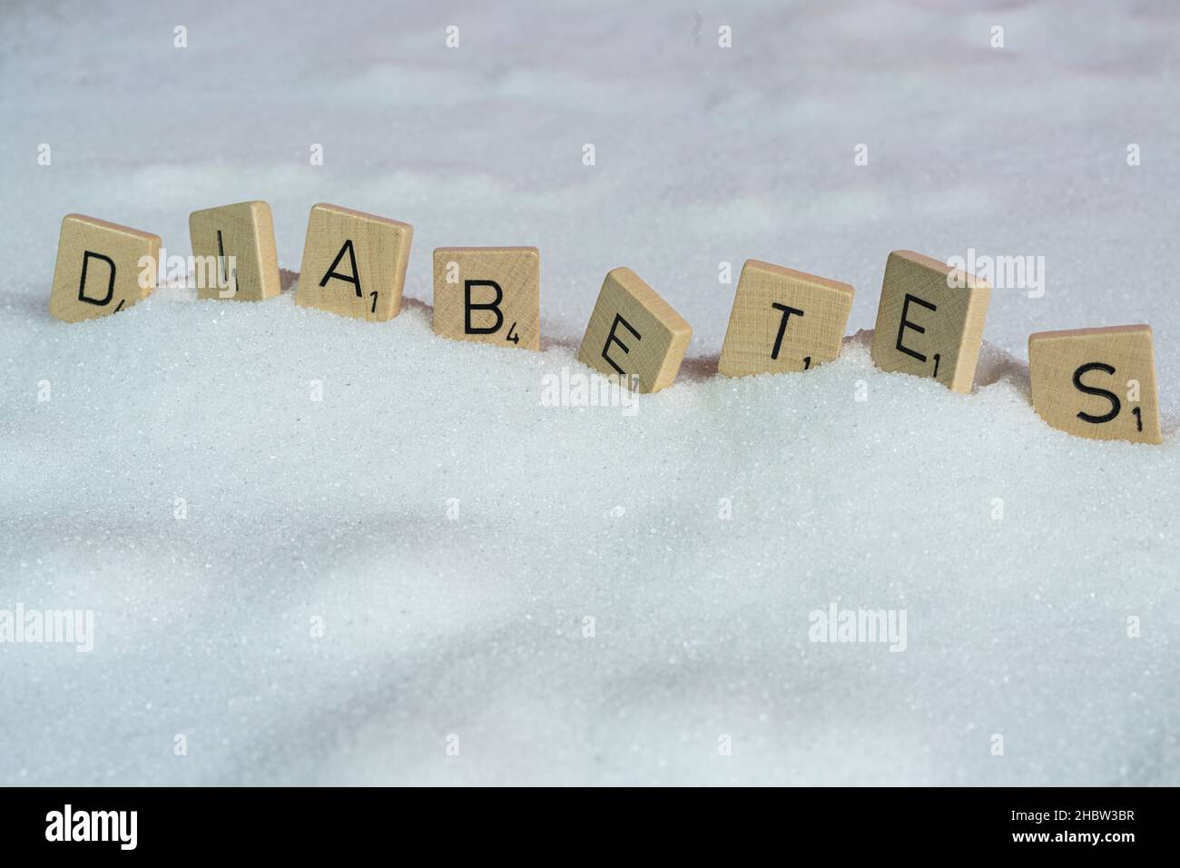 Le lettere su piccoli tasselli di legno che formano la parola diabete su una distesa di zucchero Foto Stock