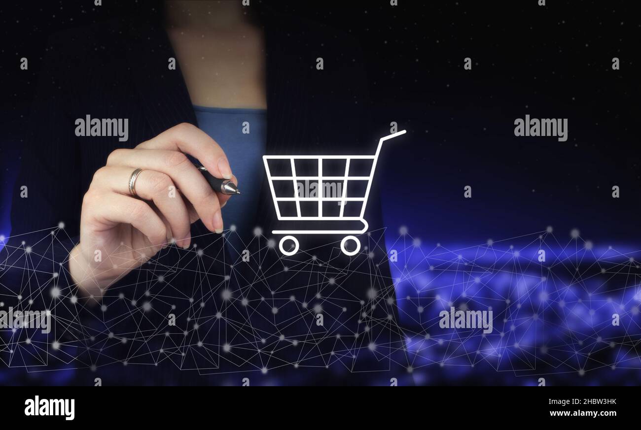 Shopping online business tecnologia internet concetto. Mano che tiene la penna grafica digitale e disegno digitale ologramma carrello segno sulla città scuro sfocato bac Foto Stock