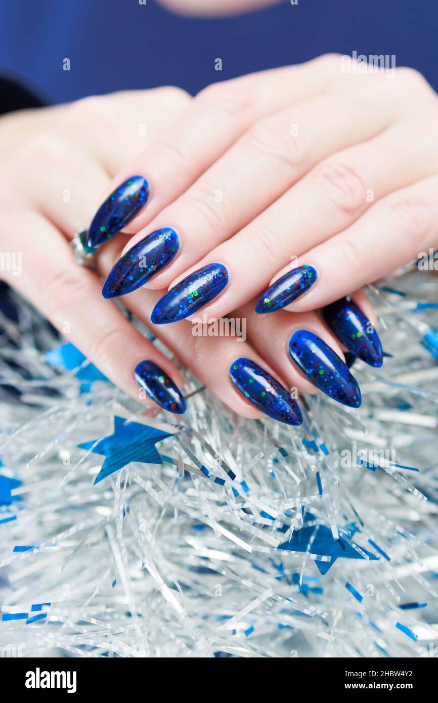 Le mani delle donne con le unghie lunghe e il manicure blu brillante  tengono una ghirlanda d'argento. Congratulazioni a Capodanno e Natale Foto  stock - Alamy