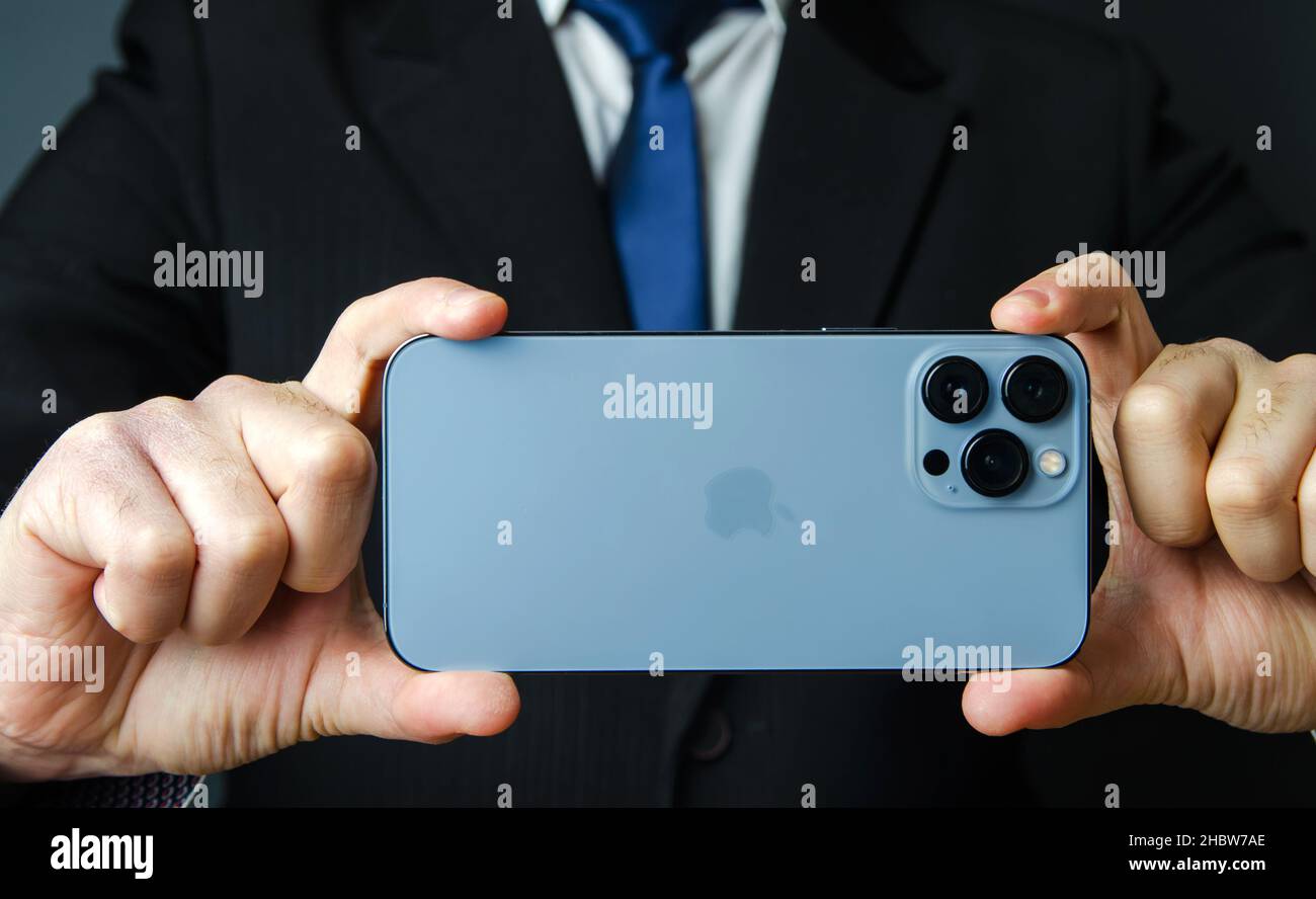 Kherson, Ucraina, 2 dicembre 2021: IPhone 13 pro max di colore blu nelle mani di un uomo d'affari. Comunicazione nel mondo degli affari, del lavoro online e dello shopping Foto Stock