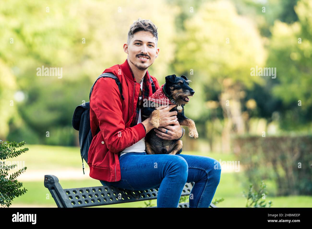 Giovane uomo con un cane seduto su una panca mentre si affaccia sulla macchina fotografica Foto Stock