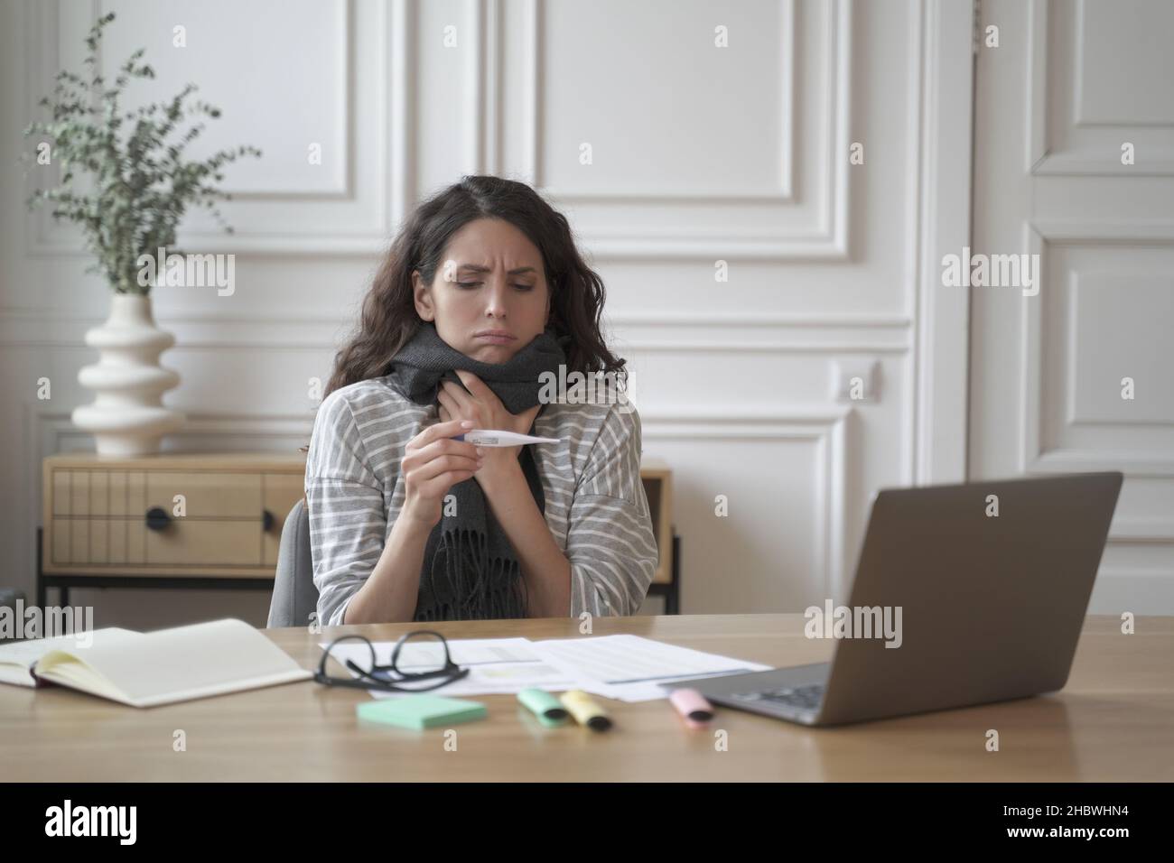 Malato giovane ispanica donna ufficio lavoratore seduto sul posto di lavoro con termometro Foto Stock