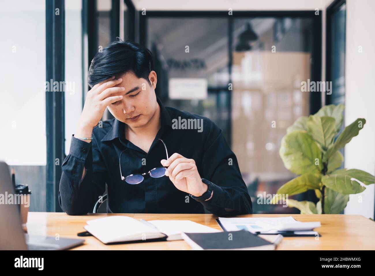 Ritratto di stressato businessman seduto alla scrivania e take off occhiali Global problemi economici concetto. Foto Stock
