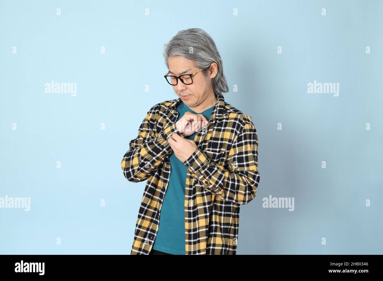 L'uomo asiatico senior con camicia a quadri gialla in piedi su sfondo blu. Foto Stock