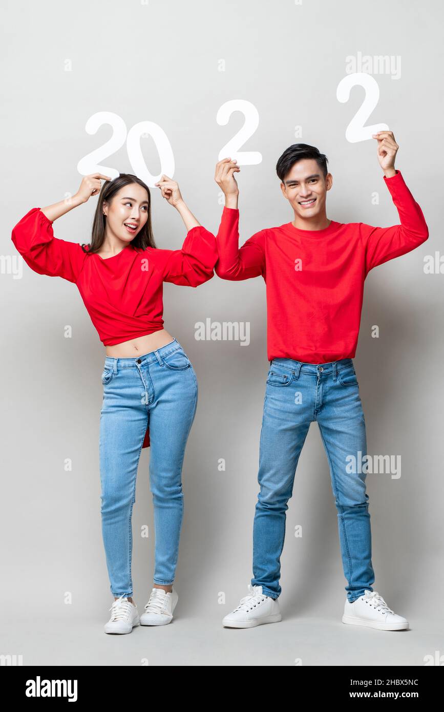 Ritratto a tutta lunghezza di felice coppia asiatica sorridente e alzante mani con numero 2022 per il nuovo anno concetto su sfondo grigio chiaro studio Foto Stock