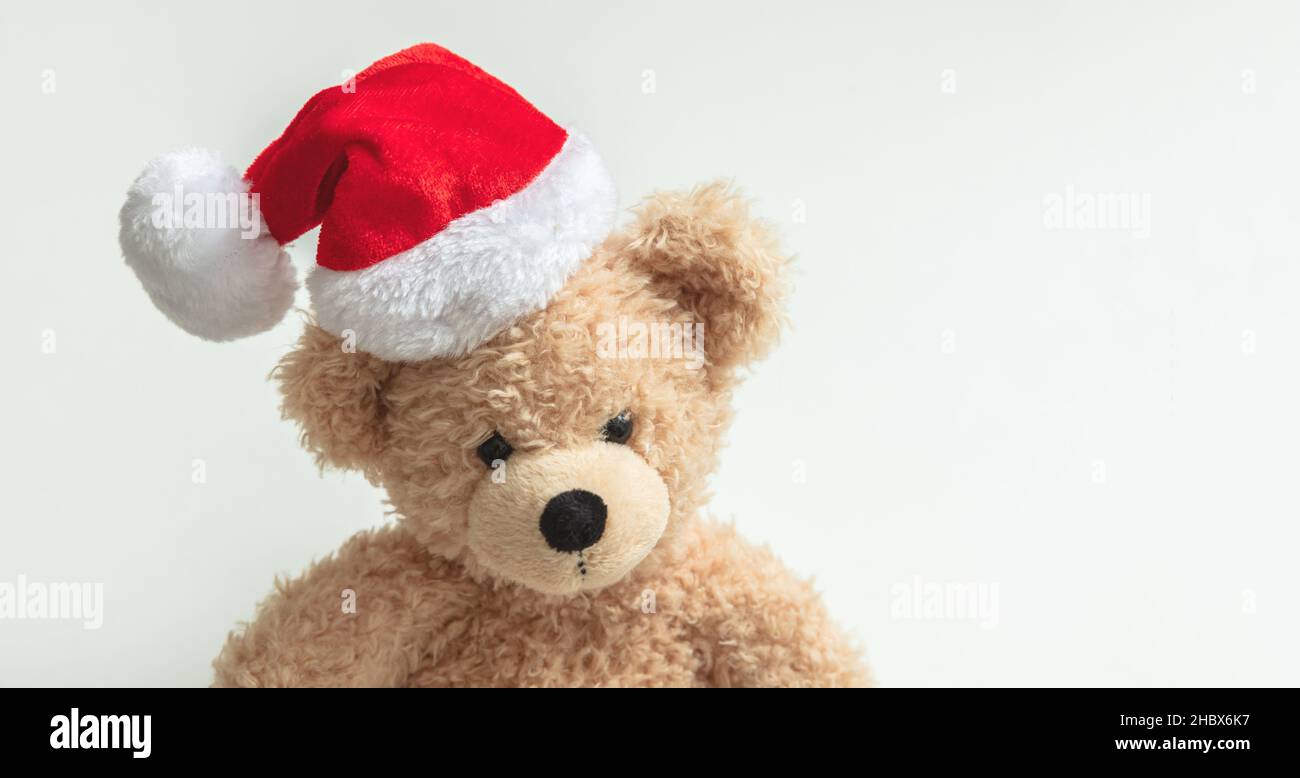 Regalo di Natale. Orsacchiotto che indossa il cappello di Santa su sfondo bianco, regali per le vacanze dei bambini, giocattoli e animali ripieni. Biglietto di auguri per le festività. Foto Stock