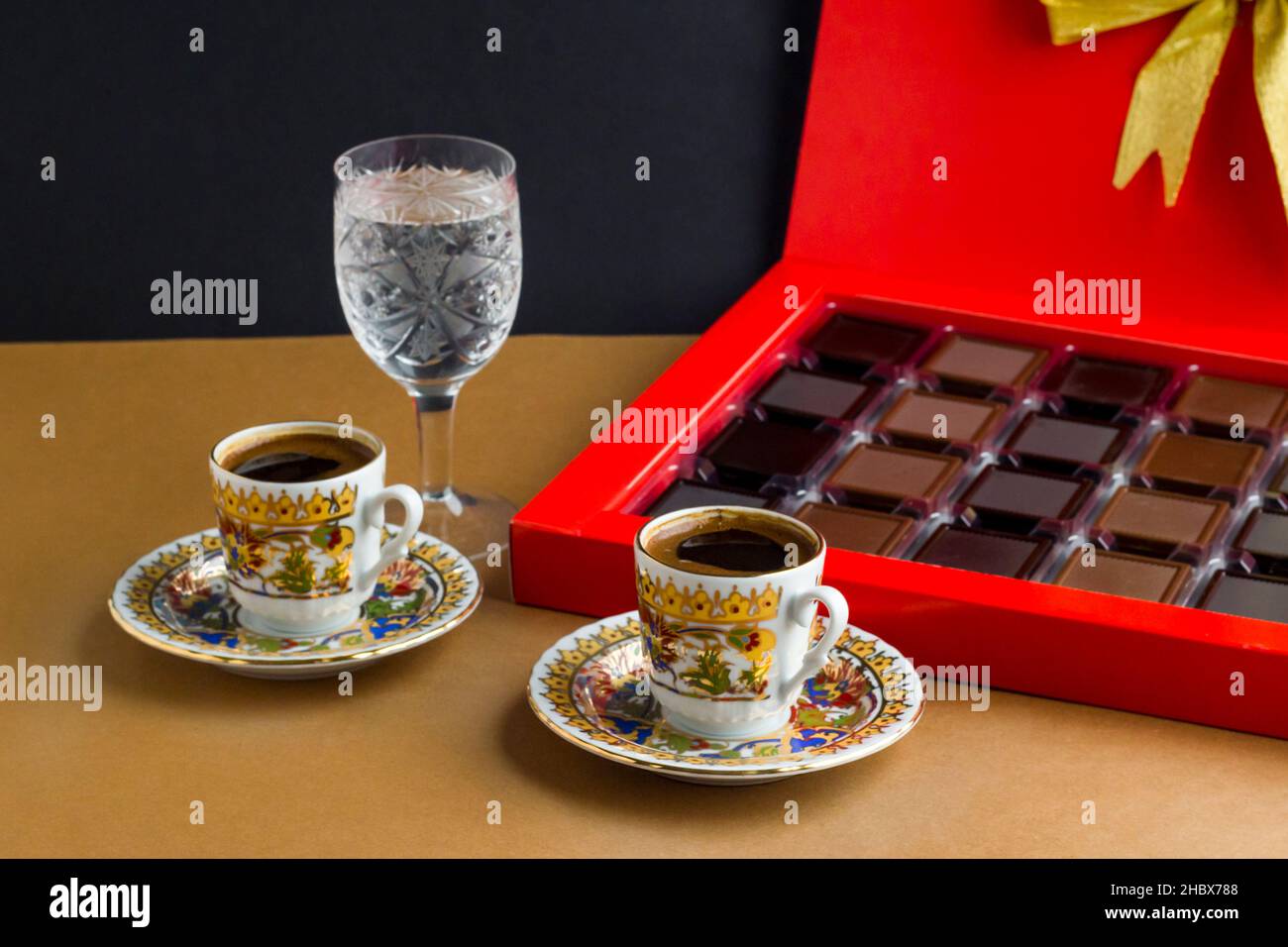 Caffè turco tradizionale in tazze dorate, sulla superficie marrone con cioccolato madlen e un bicchiere di acqua.immagine concettuale per ogni festa. Foto Stock Caffè turco tradizionale in tazze dorate, sulla superficie marrone con cioccolato madlen e un bicchiere di acqua.immagine concettuale per ogni festa. Foto Stock