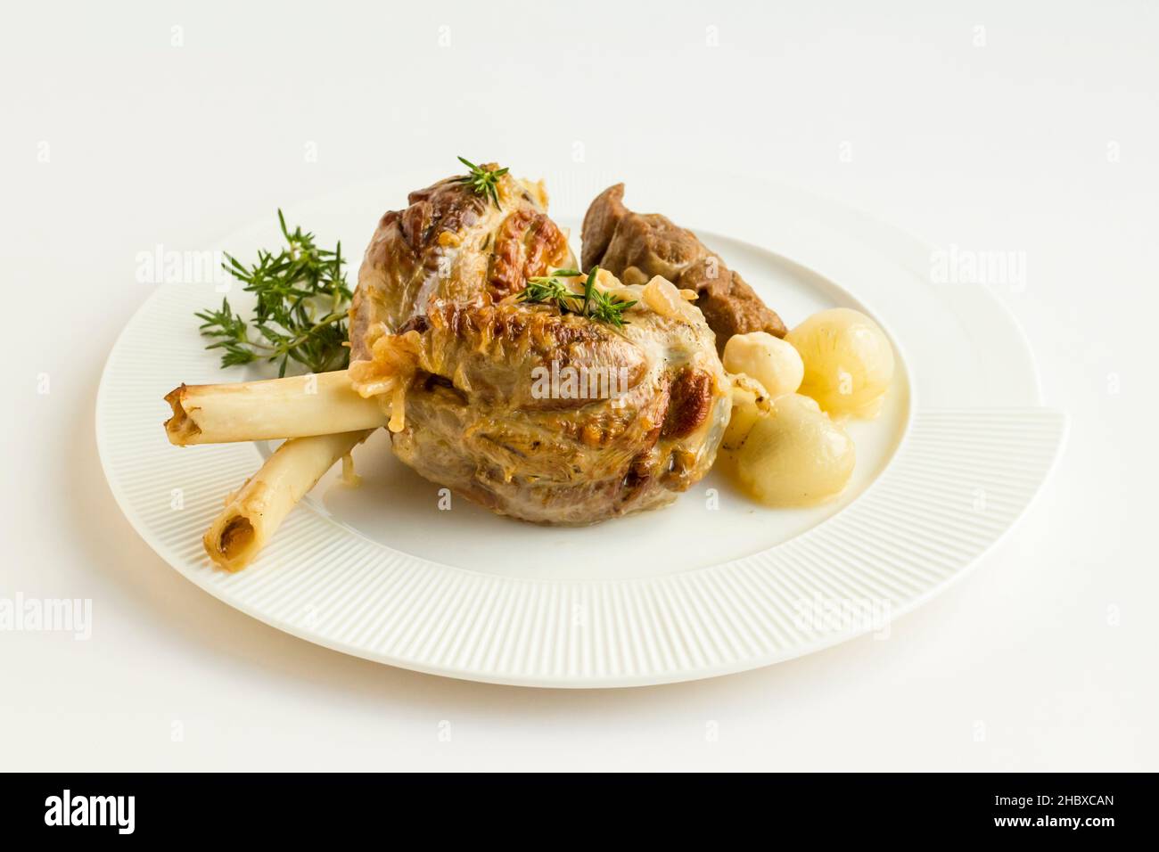 Ben cotti tre pezzi di stinco di agnello in piatto bianco con timo fresco, Unione e aglio. Il Sacrifice Festival Food Foto Stock