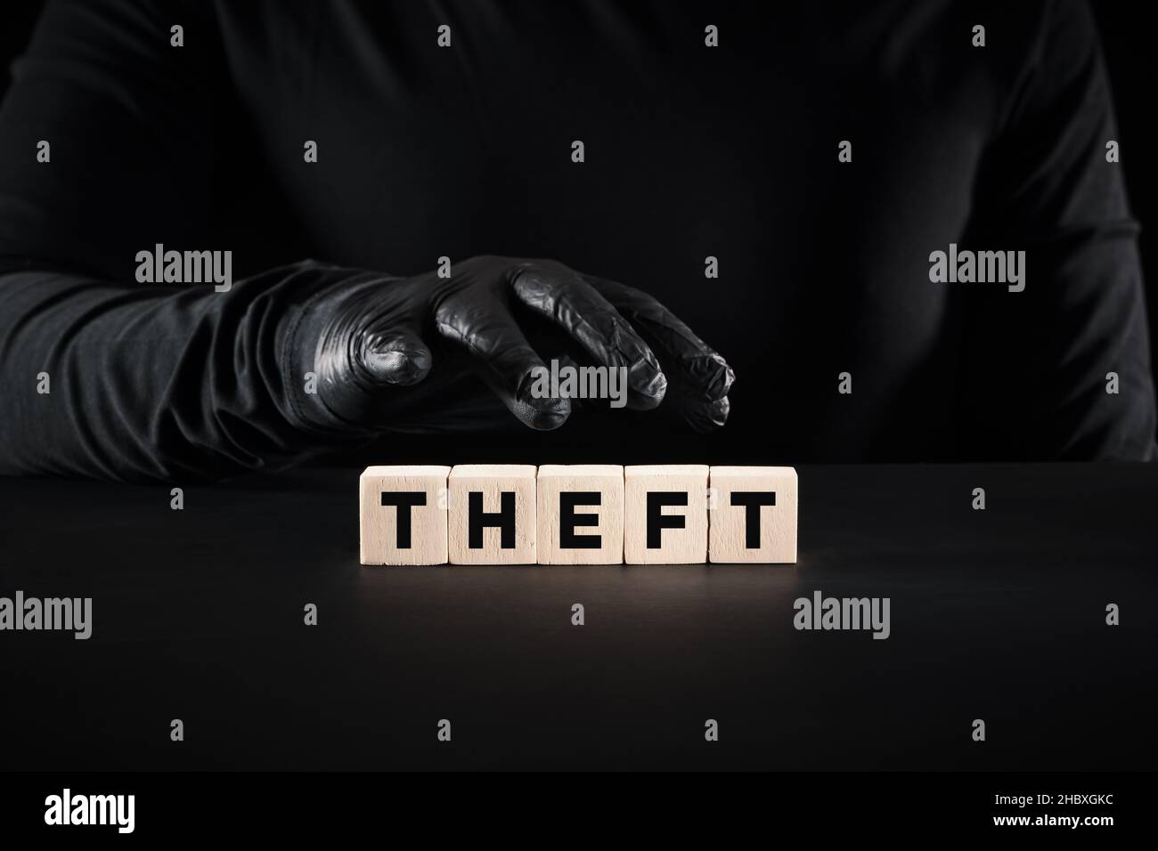 Furto, crimine, furto o furto. La mano criminale che indossa guanti neri è sopra i blocchi di legno con la parola furto. Foto Stock