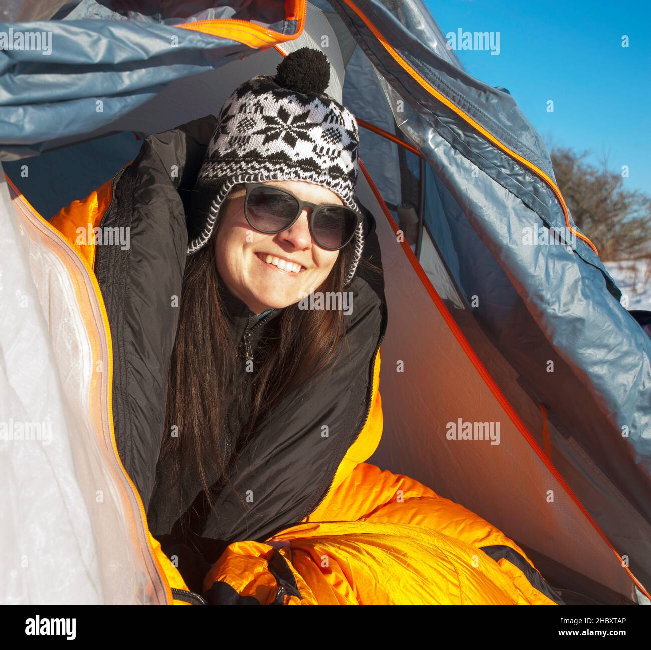 Donna che guarda dalla tenda patta sorridente indossare cappello invernale. Foto Stock