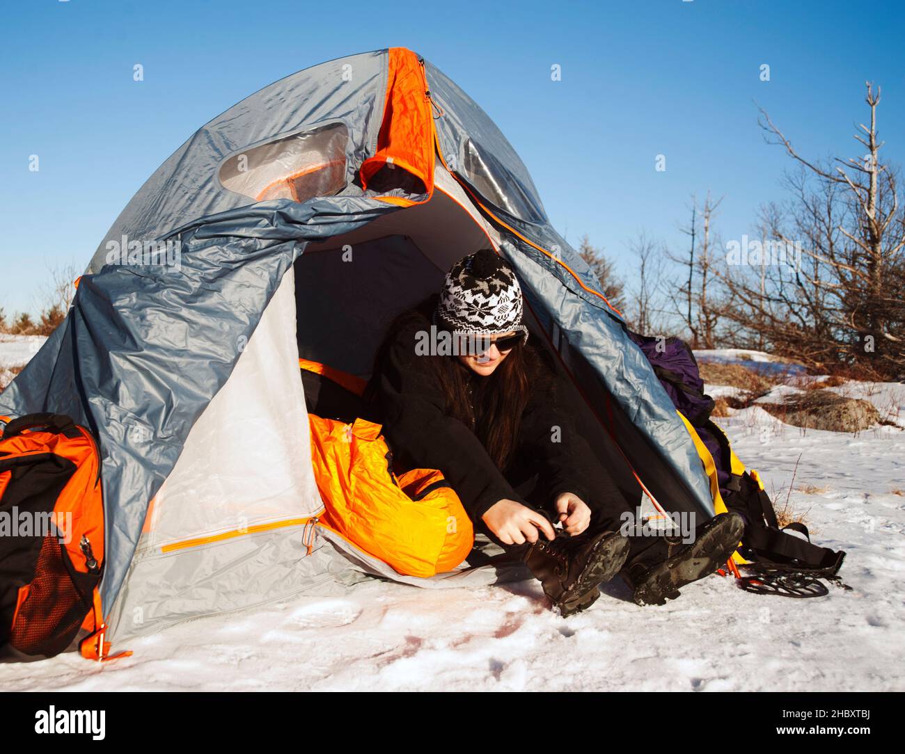 Donna seduta in tenda in paesaggio nevoso allacciando scarponi da neve. Foto Stock