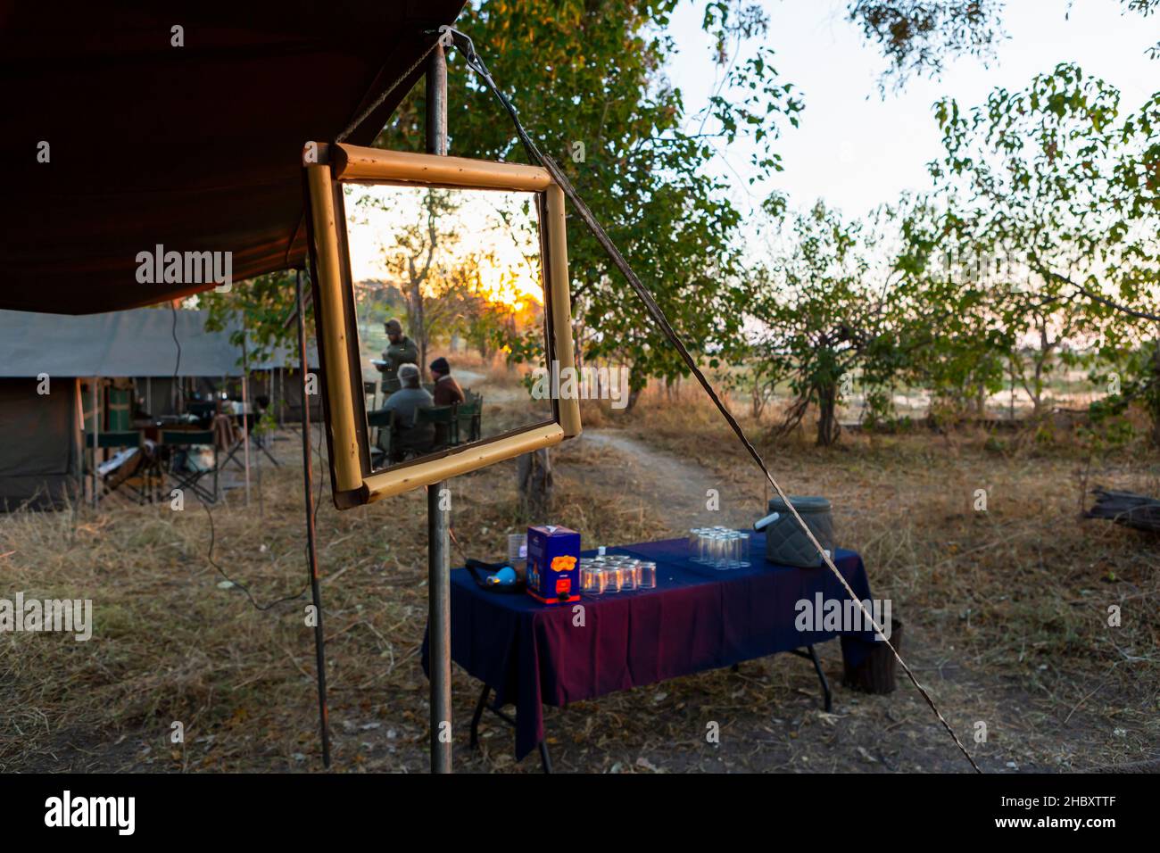 Un campo safari, tende e bevande tavolo, un grande specchio su una tenda palo, tre persone al tramonto Foto Stock