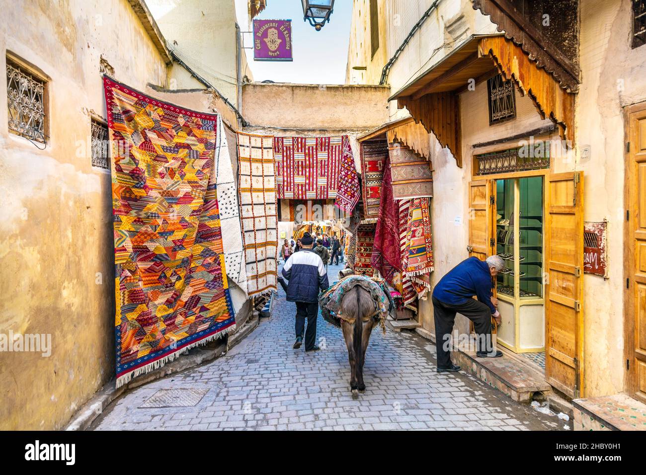 Uomo che cammina con asino, strada stretta nei souk della medina con negozi di tappeti marocchini, Fes, Marocco Foto Stock