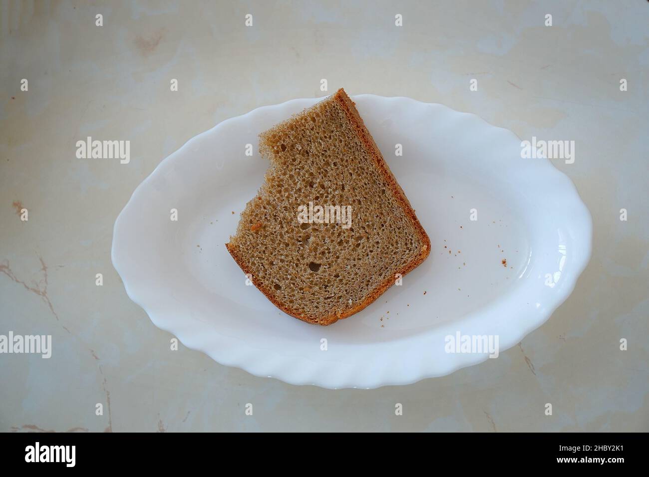 Metà-mangiato pezzo di pane di segale su piatto bianco Foto Stock
