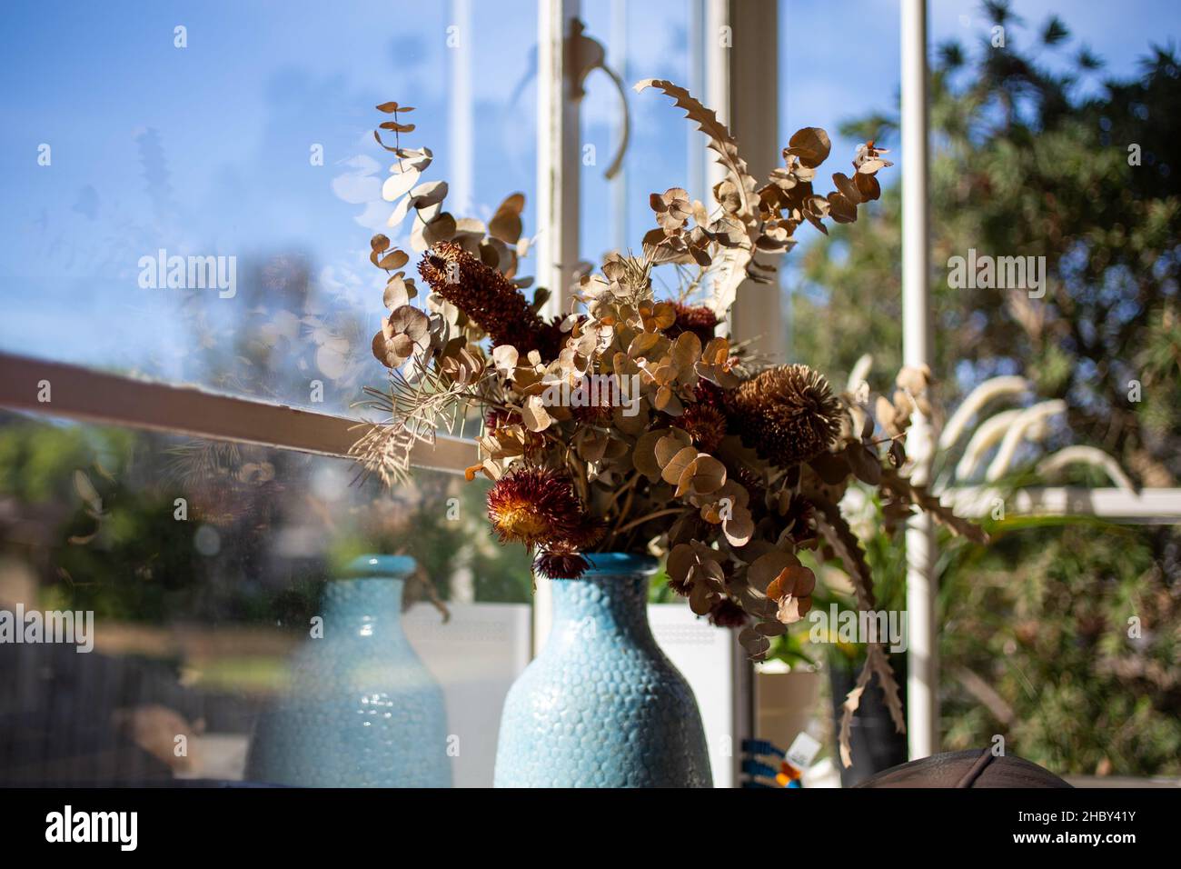 Un bel bouquet con fiori secchi in vaso blu davanti a una finestra Foto Stock