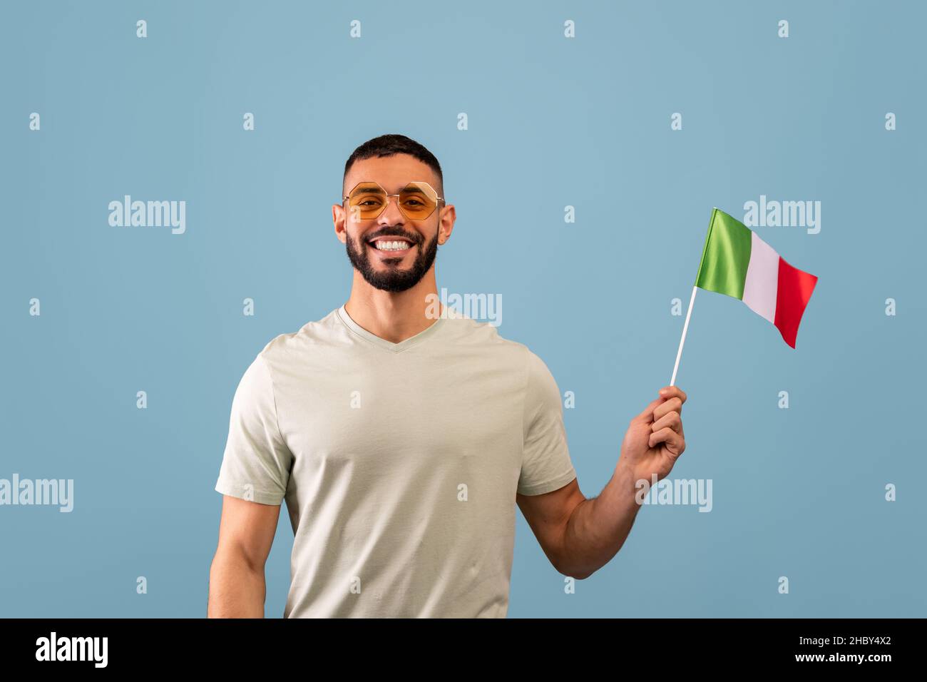 Un ragazzo arabo positivo che mostra la bandiera d'Italia, posando su sfondo blu e sorridendo alla fotocamera. Concetto dei corsi di lingua Foto Stock