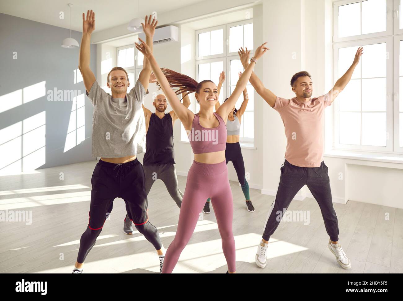 Gruppo di giovani felici che fanno jumping jacks durante un allenamento cardio in palestra Foto Stock