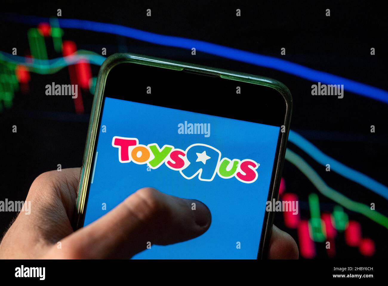 In questa illustrazione della foto il logo della catena di giocattoli multinazionale americana ToysRus (Toys 'R' US) visto su uno smartphone con un grafico di indice di borsa economica sullo sfondo. Foto Stock