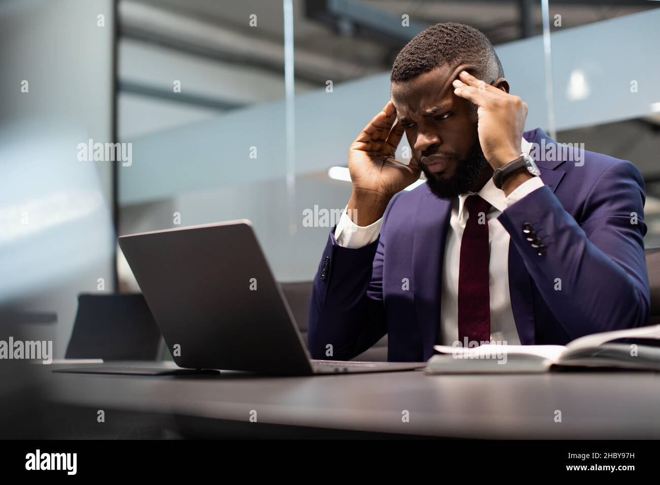 Un uomo d'affari nero concentrato che risolve le attività aziendali, utilizzando il computer Foto Stock