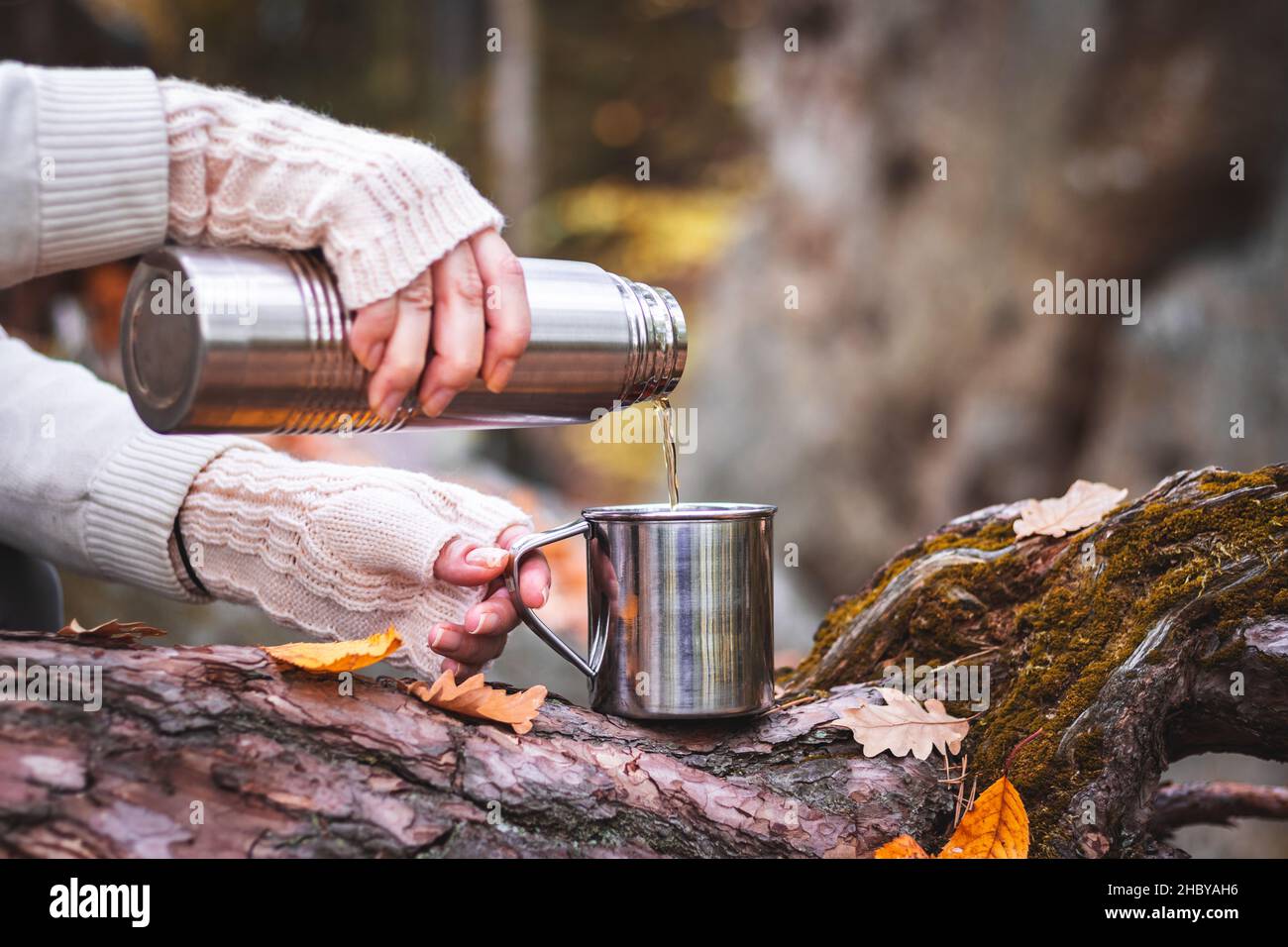 Donna con guanto in maglia versa una bevanda calda in tazza da thermos. Rinfresco durante le escursioni. Foto Stock
