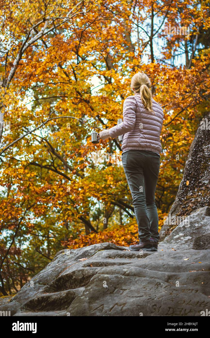 Viaggiando donna che tiene la tazza e thermos con la bevanda calda e guardando alla foresta d'autunno. Rinfresco durante le escursioni. Foto Stock