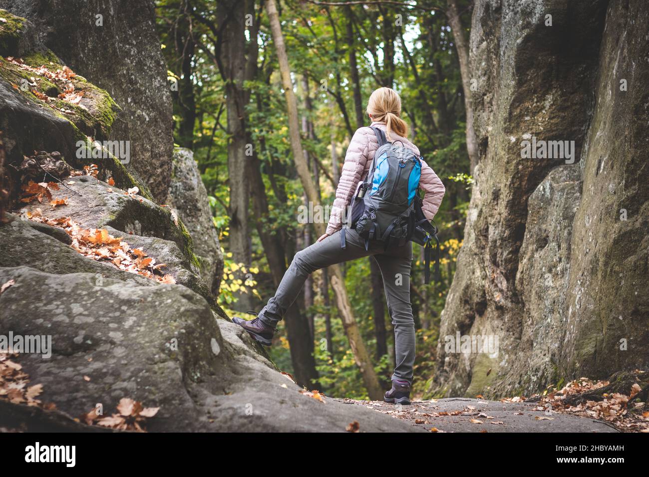 Donna con zaino che viaggia nella foresta. L'escursionista femminile è in piedi tra le rocce in montagna. Foto Stock