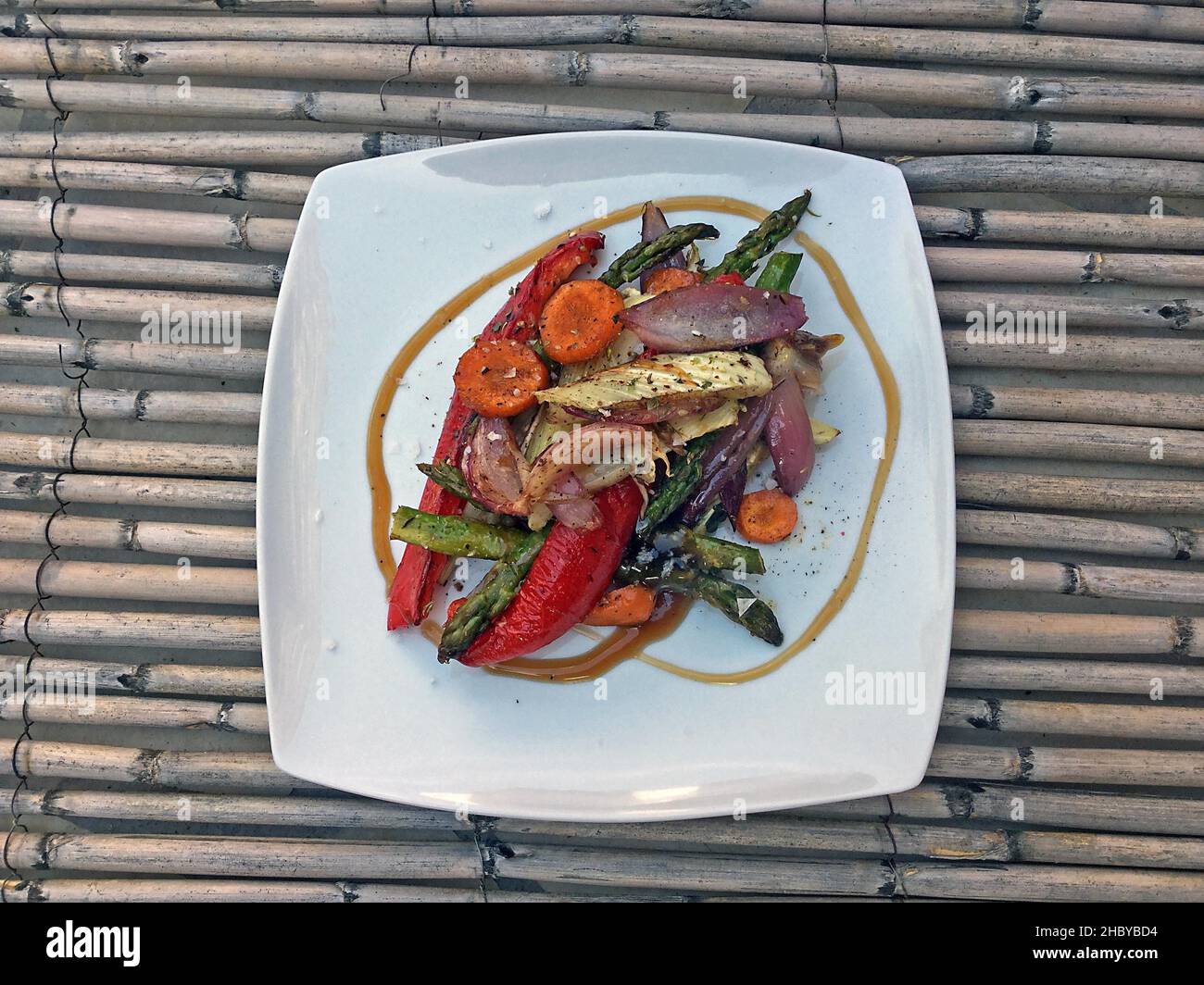 Verdure da forno a piastra bianca su stuoia di paglia con carote, pepe rosso, asparagi verdi e cipolle Foto Stock