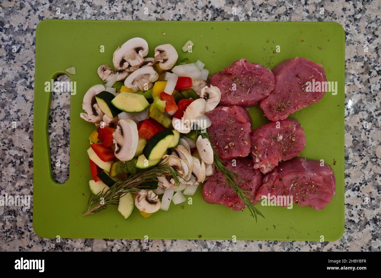 Filetti di maiale crudo con funghi a fette e zucchine su una tavola verde, vista dall'alto, dall'alto Foto Stock