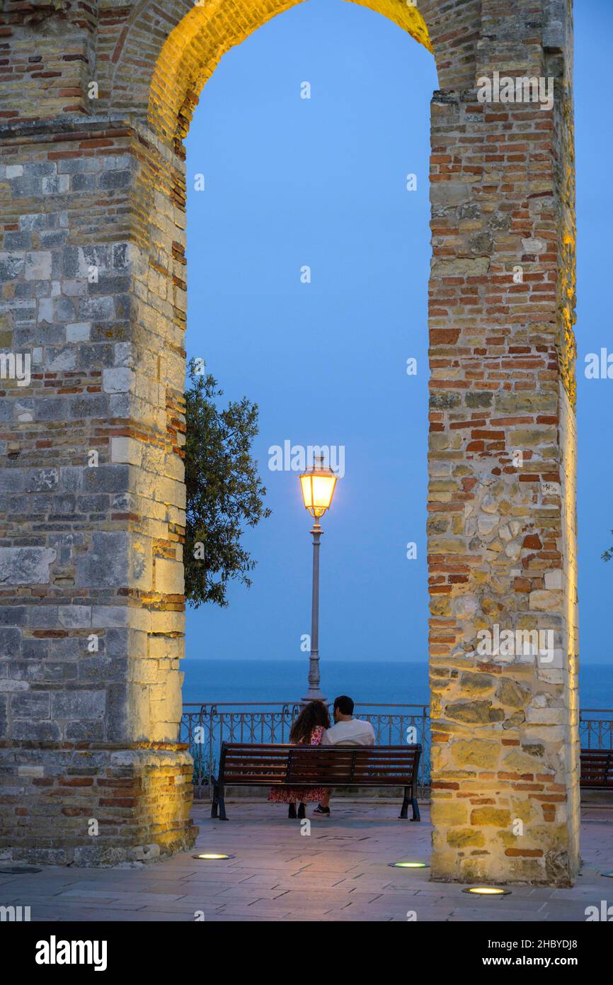 Antica arcata al Belvedere e coppia seduta su una panchina che guarda al mare, Numana, provincia di Ancona, Italia Foto Stock