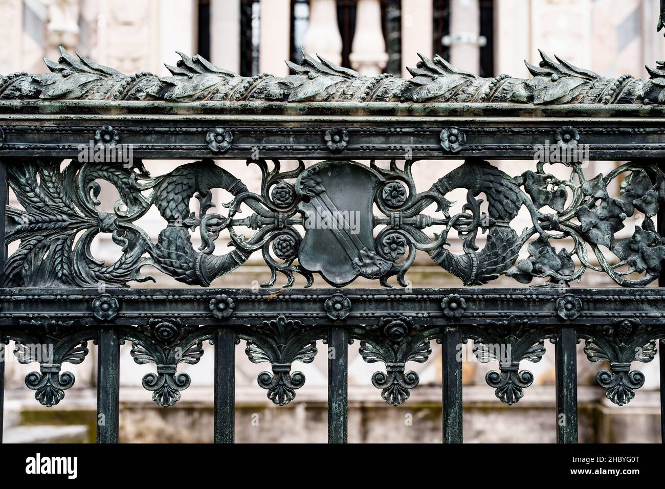 Antica recinzione in ferro battuto nei pressi del Duomo di Milano con guglie, scudi, fiori e ricci Foto Stock