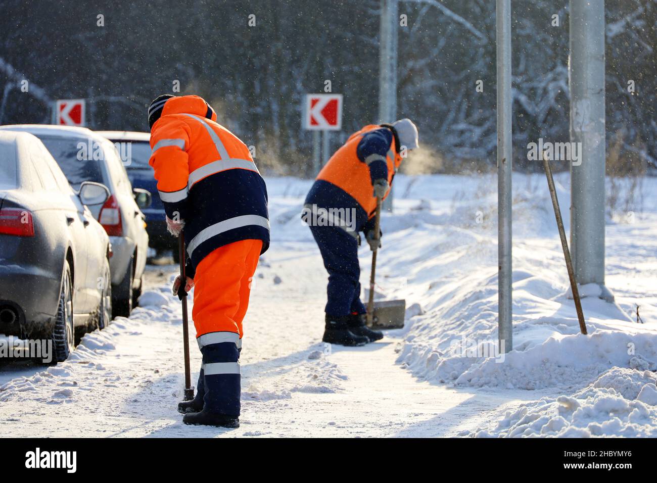 Rimozione della neve in città d'inverno alle basse temperature. Due uomini lavoratori in uniforme con una pala e crowbar pulizia della strada vicino al parcheggio auto Foto Stock