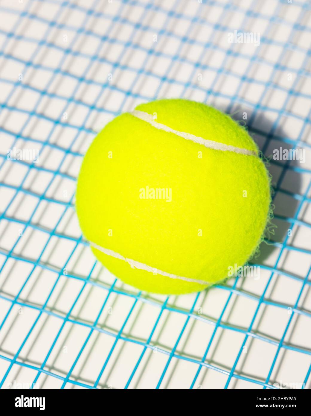 Una palla da tennis gialla sulle corde blu di una racchetta da tennis su sfondo bianco. Composizione sportiva Foto Stock