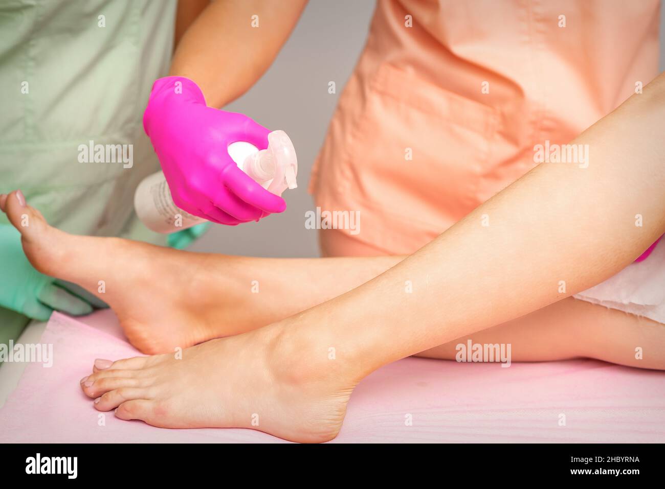 Un estetista spruzza un disinfettante sui piedi di una giovane donna prima della procedura di epilazione. Depilazione del piede Foto Stock