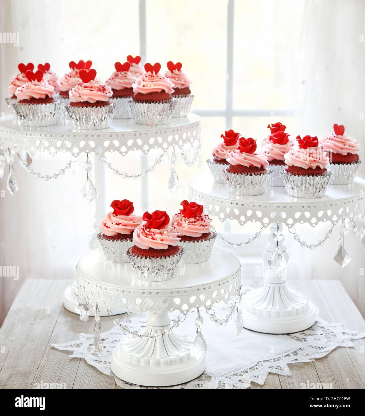 Cupcake in velluto rosso con glassa di vaniglia rosa decorata con rose rosse su uno stand a tre piani. Foto Stock