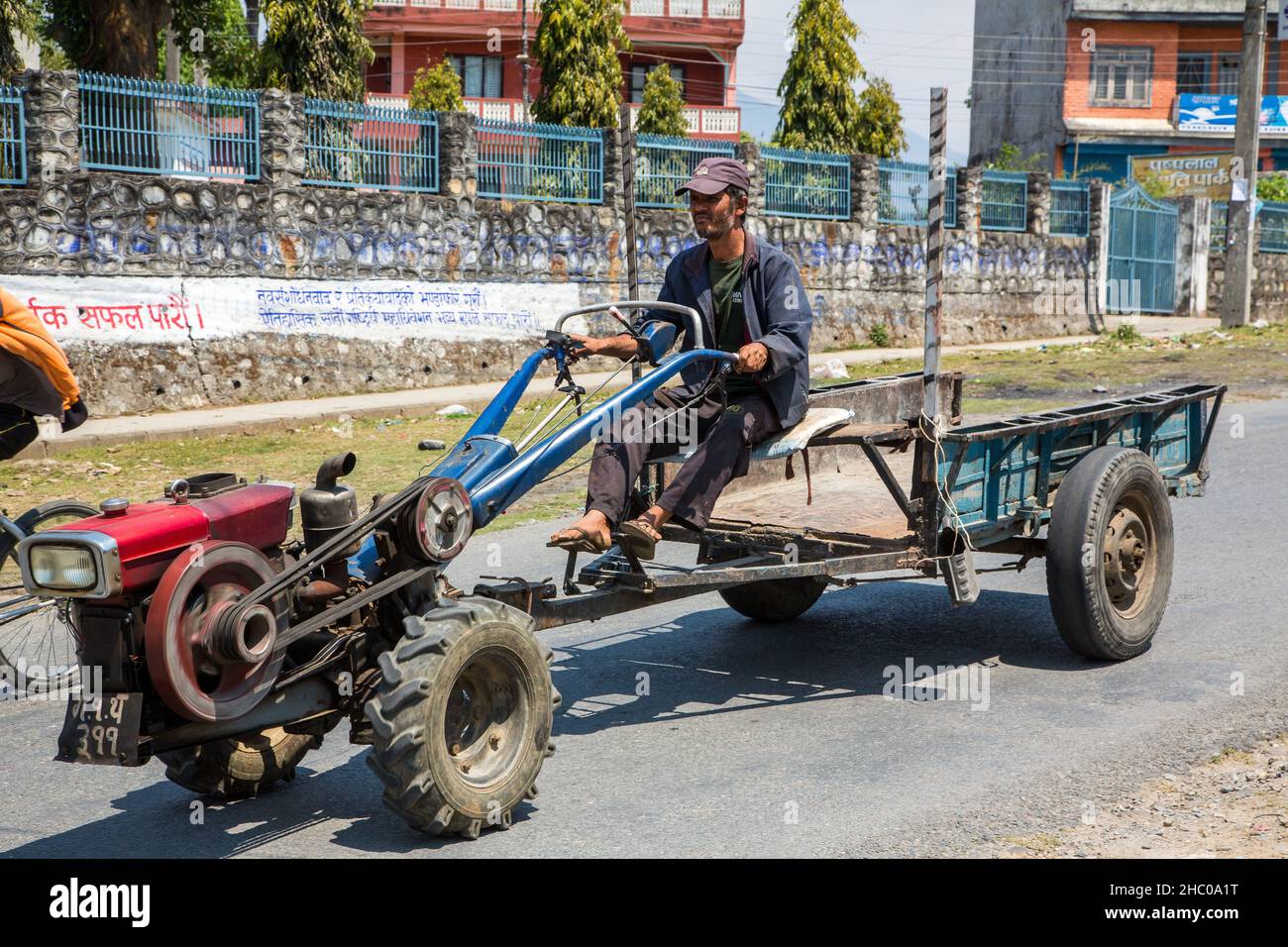 Un uomo guida un trattore a due ruote con un rimorchio su una strada a Kathmandu, Nepal. Foto Stock