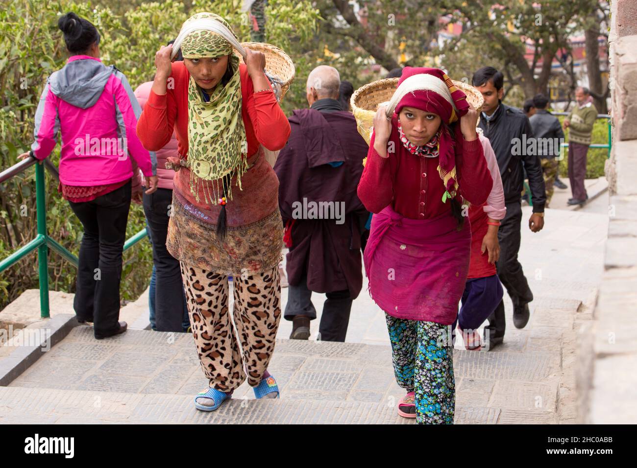 Due giovani donne nepalesi trasportano pesanti cesti di pietre sulle loro spalle su scale usando una tumpline a Kathmandu, Nepal Foto Stock