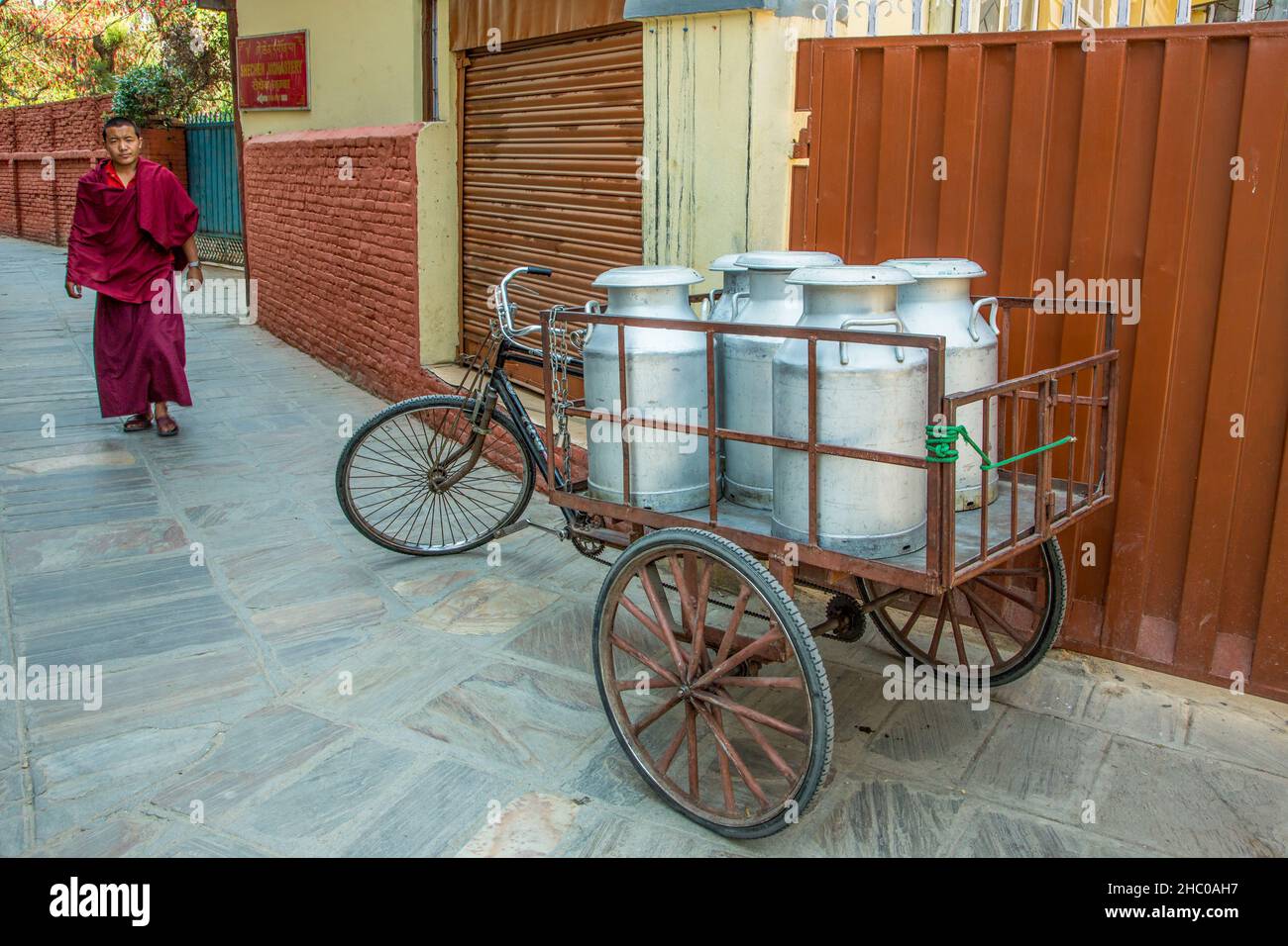 Un monaco buddista cammina lungo una strada pedonale verso un carrello di consegna triciclo vicino al monastero di Sechen, Kathmandu, Nepal. Foto Stock