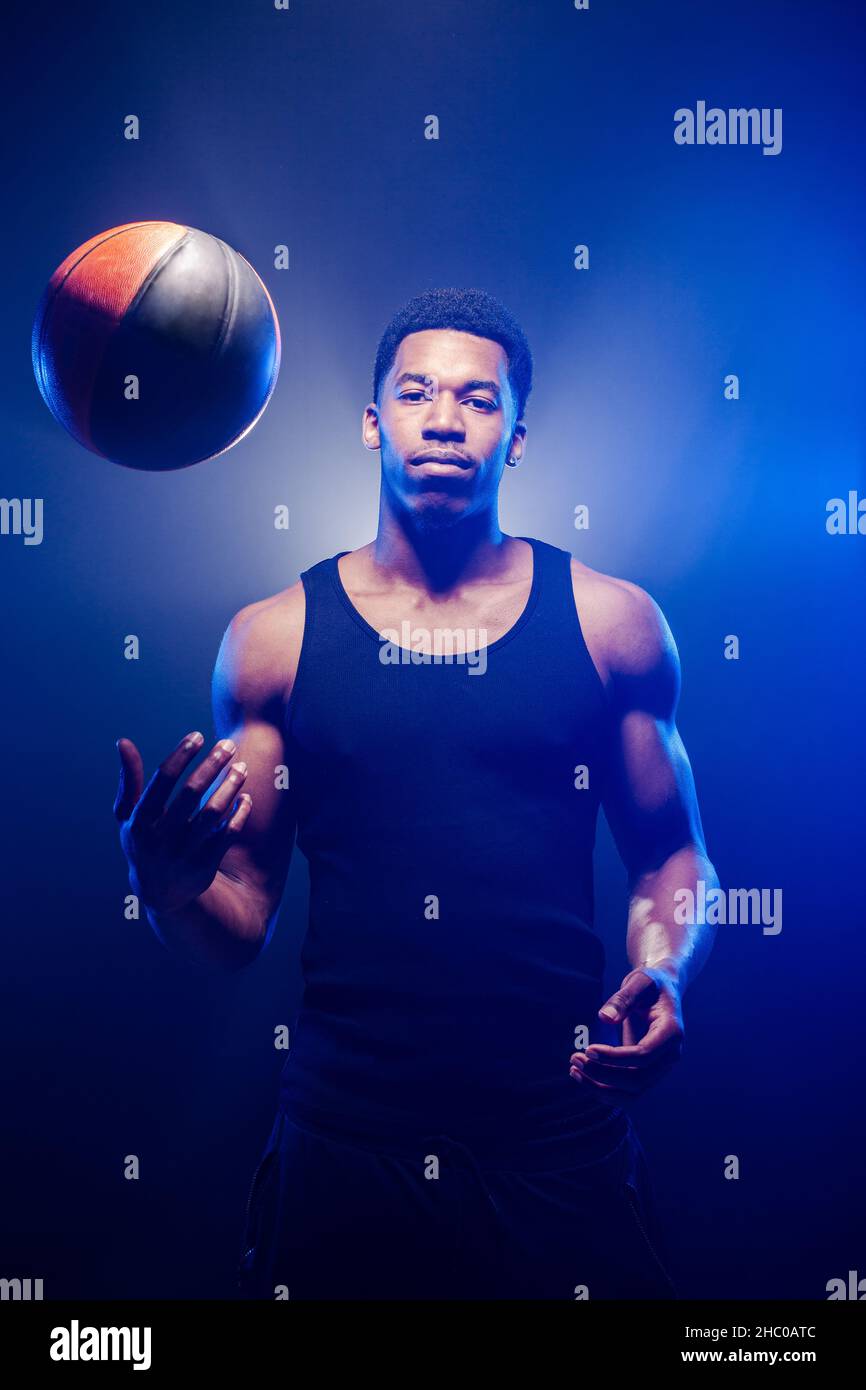 Giocatore di basket che tiene una palla contro sfondo blu nebbia. L'uomo afro-americano lancia la sfera del cestino Foto Stock