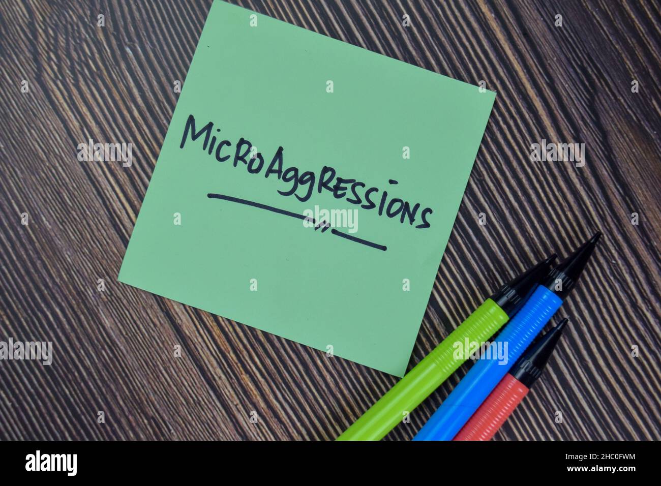 Le microaggressioni scrivono su note appiccicose isolate su tavola di legno. Foto Stock