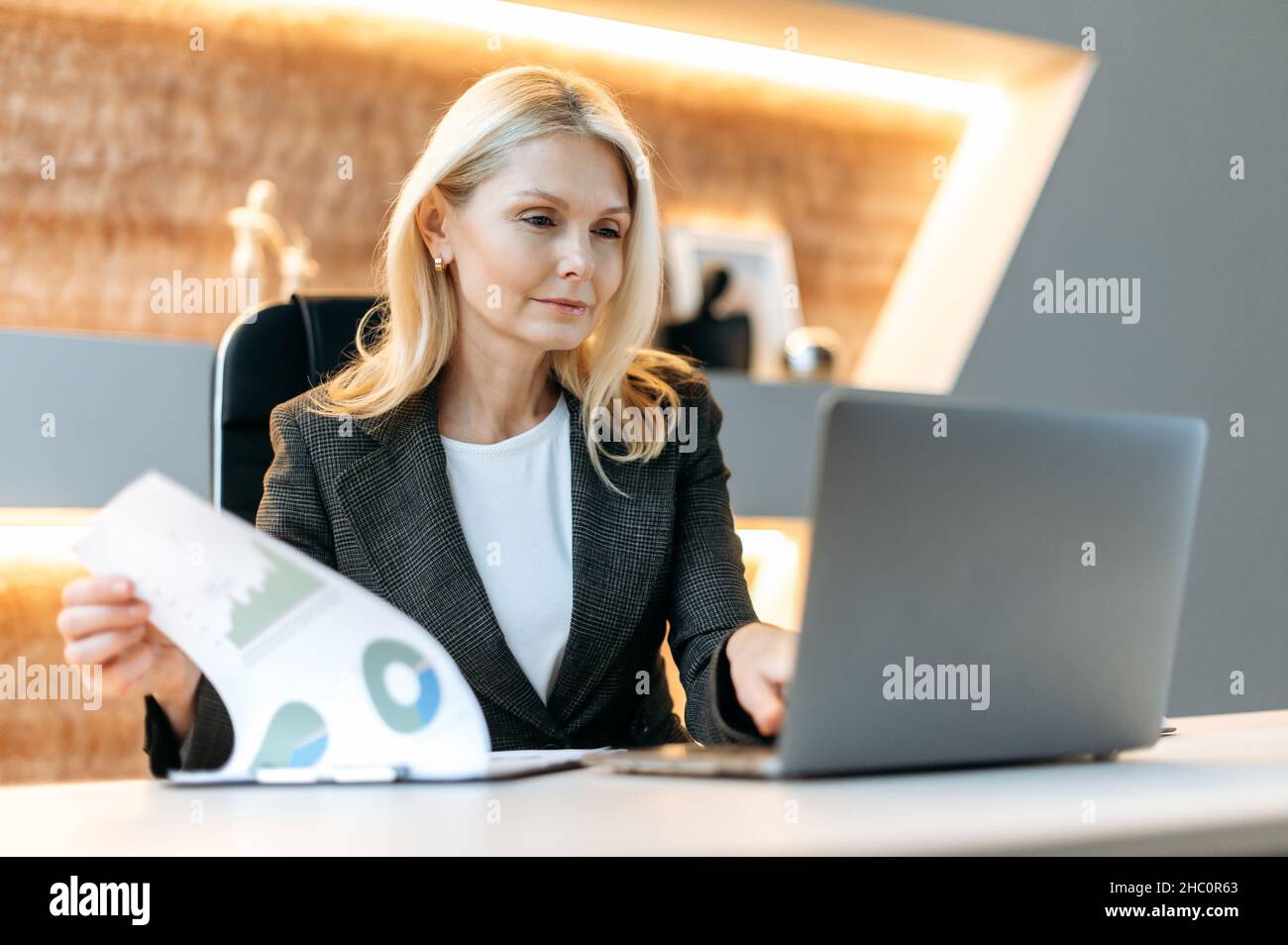 Caucasica maturo influente e di successo smart business donna, analista finanziario, manager, seduto a un laptop, studiare documenti, analizzare diagrammi e pianificare la strategia finanziaria Foto Stock
