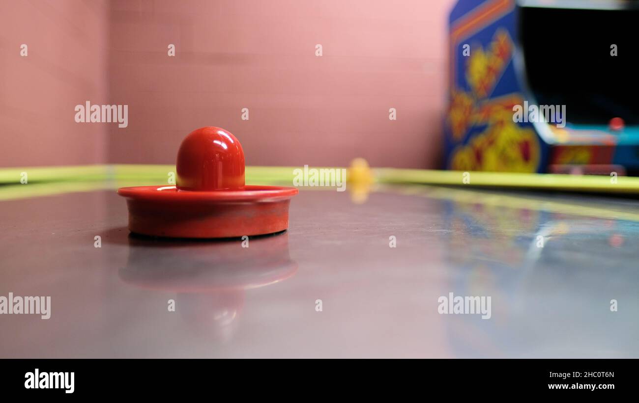 Tavolo da hockey ad aria con paddle goalie con pestello scorrevole e console di gioco MS. Pacman in background in una sala giochi e videogiochi. Foto Stock