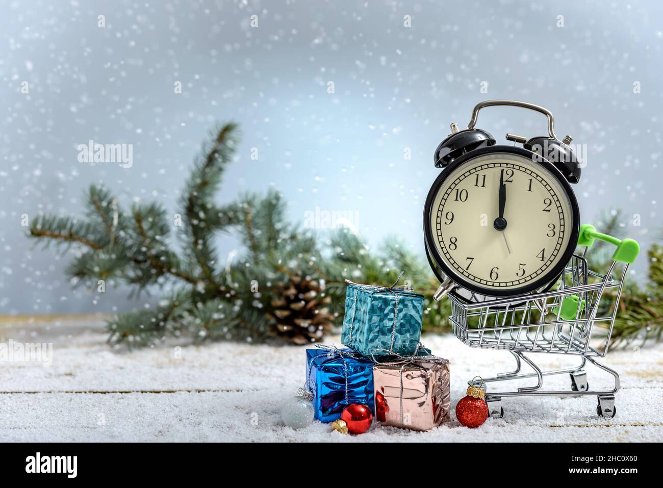 Concetto di shopping di Natale. Sveglia in un carrello e scatole regalo accanto al ramo di abete mentre sta nevicando su un tavolo di legno. Foto Stock