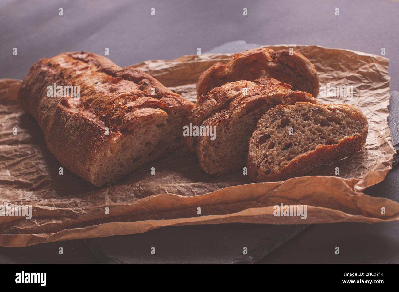 baguette di farina di grano saraceno senza lievito su sfondo nero, fette di pane affettato su carta pergamena. Foto Stock