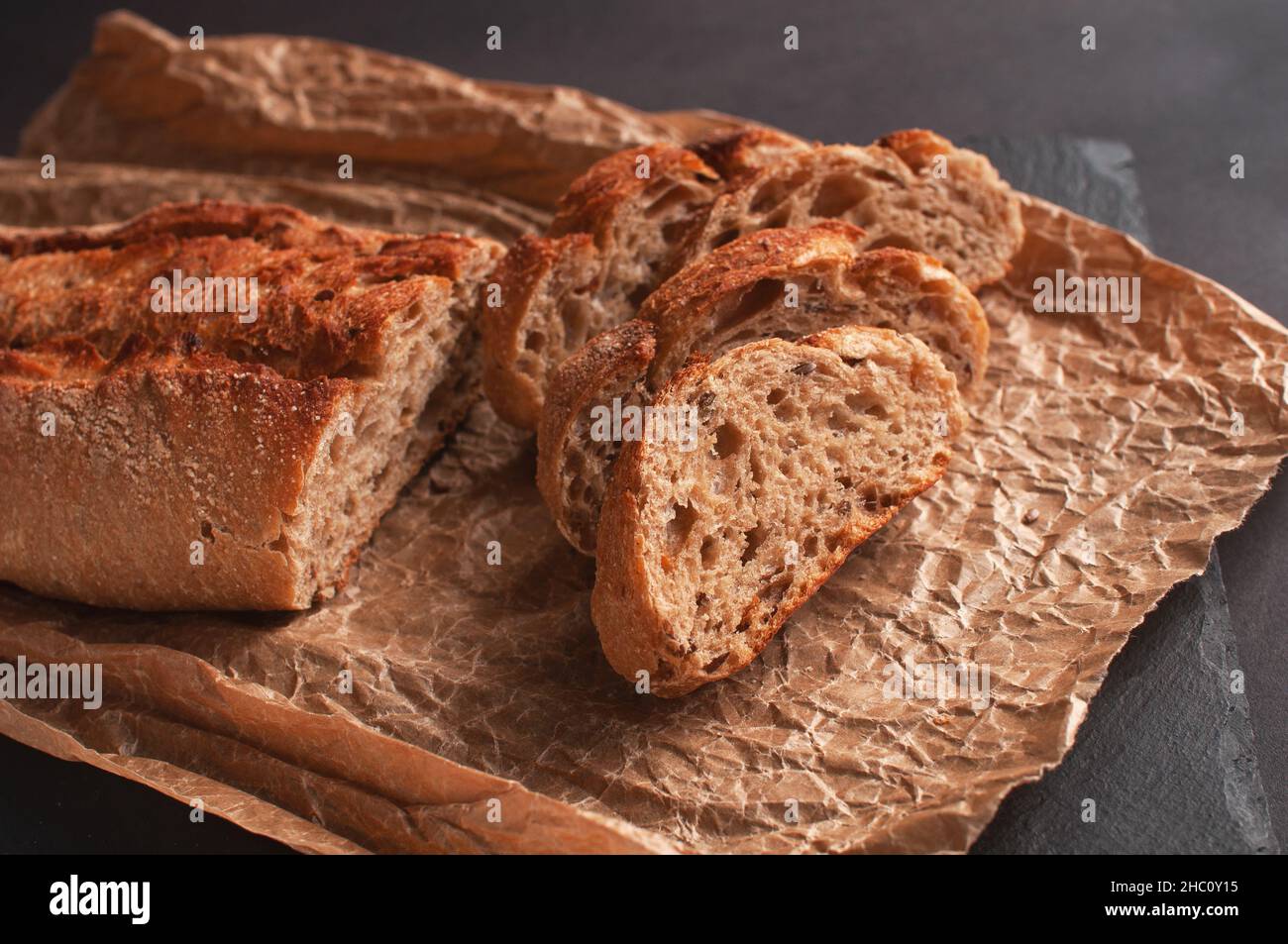 baguette di farina di grano saraceno senza lievito su sfondo nero, fette di pane affettato su carta pergamena. Foto Stock