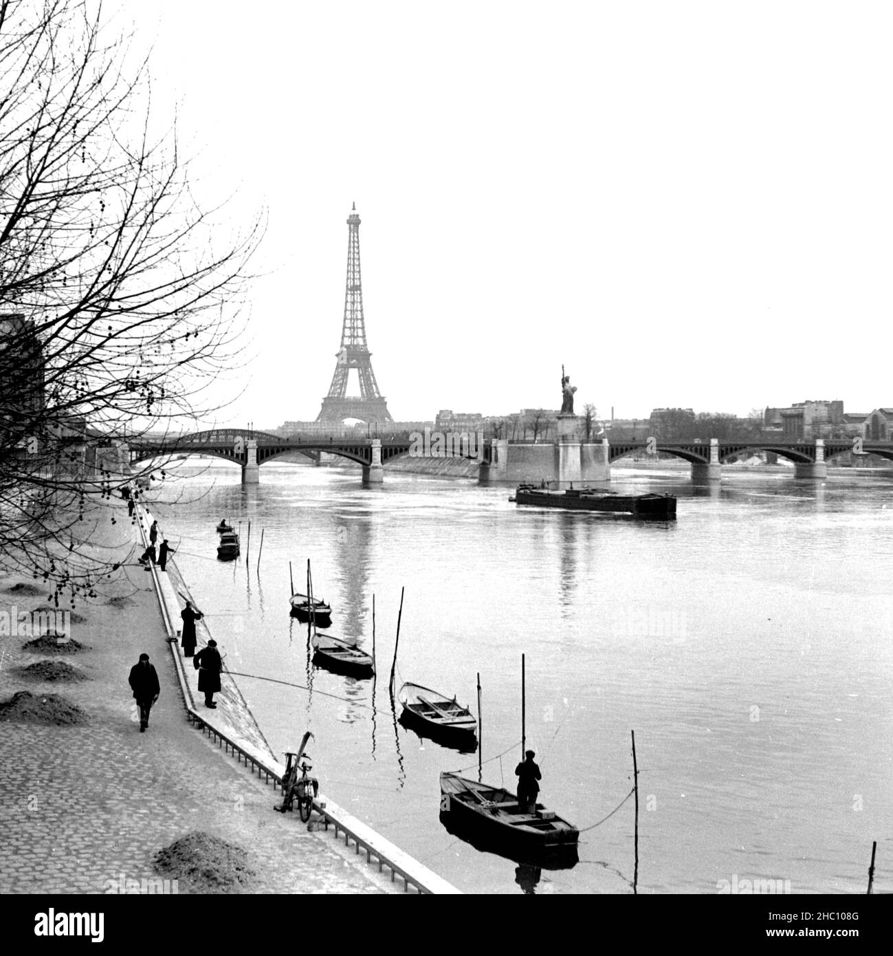 Parigi pescatori sulla Senna - foto da Pont Mirabeau, dicembre 1944. Uomini con pali lunghi pescano dalla banca o dalle barche. Nelle vicinanze sul fiume ci sono barche a sette file; l'avvicinamento è una chiatta. La Statua della libertà Petite è di fronte alla macchina fotografica da Pont de Grenelle. Alle spalle si vedono il Pont de Bir Hakeim e la Torre Eiffel. Mucchi di foglie rastrellate costeggiano la vicina riva del fiume. Foto Stock